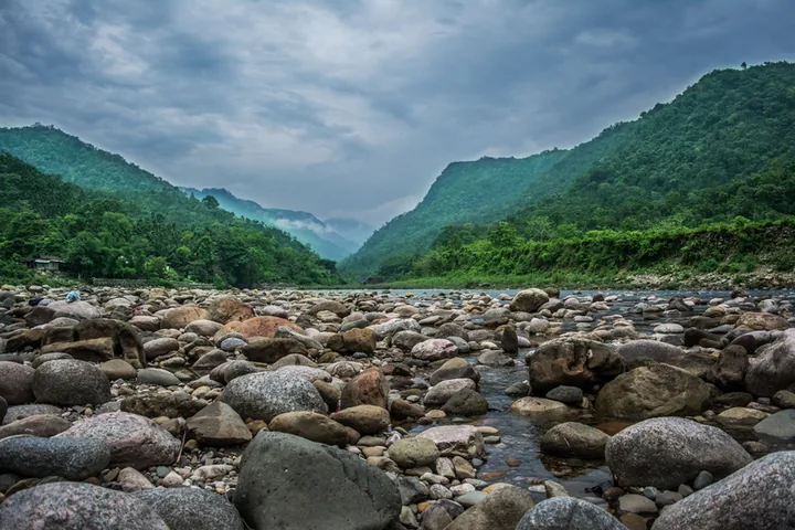 White stones in the river at Bholaganj with green hills behind